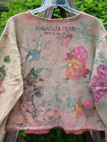 Magnolia Pearl Fleece Lucky Anna Glitter Sweatshirt Marais OSFA, showcasing MAGNOLIA PEARL LOVE SUPPLY CO., whimsical cat and bird, roses, and deliberate distressing for a vintage, bohemian charm, hanging outdoors.