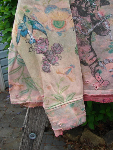 Magnolia Pearl Fleece Lucky Anna Glitter Sweatshirt Marais OSFA draped over a wooden post, showcasing its distressed vintage-washed look with faded floral, bird, and animal motifs, complete with frayed edges.