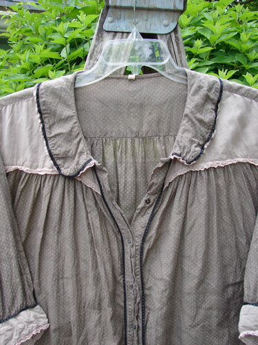 Magnolia Pearl Silk Cotton Poet's Billow Blouse features a billowy, gathered yoke with ruffled trim, lace-accented collar, and polka dot backdrop, hanging on a clear hanger against leafy shrubs.