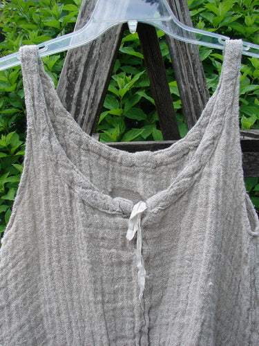 Magnolia Pearl Fisherman's Weave Ribbon Neck Top Flaxen OSFA displayed on a clear hanger, showcasing its loose, airy basket weave and scalloped hem with weighted ruffles against a natural, leafy backdrop.