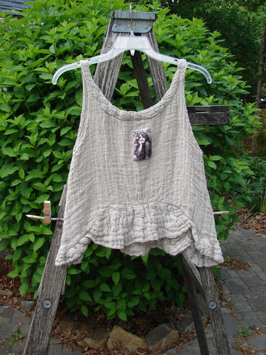 Magnolia Pearl Fisherman's Weave Ribbon Neck Top Flaxen OSFA, displayed on a wooden ladder, features a crinkled cotton texture, ruffled hem, and a classical statue bust patch on the chest.