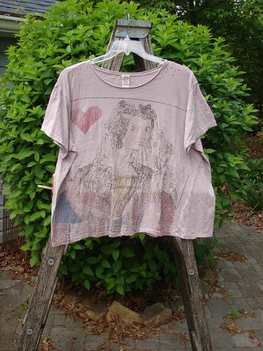 Magnolia Pearl Cotton Jersey Boyfriend Tee Queen of Hearts Pink Dust OSFA draped over a wooden stand, showcasing its large playing-card motif, distressed fabric with holes, and flutter edges against a natural backdrop.