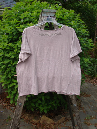Magnolia Pearl Cotton Jersey Boyfriend Tee Queen of Hearts Pink Dust OSFA hangs on a stepladder, showcasing its super soft, drapey feel, flutter edges, and signature back stamp against lush greenery.