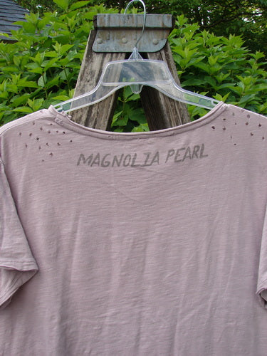 Magnolia Pearl Cotton Jersey Boyfriend Tee Queen of Hearts Pink Dust OSFA features intentional distress holes, upper shoulder distressing, flutter edges, and a distinctive rear Magnolia Pearl signature against a wooden frame backdrop.