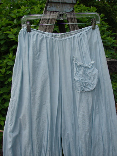 Magnolia Pearl Silk Voile Window Lace Ruffle Pocket Bloomer Sky OSFA with elastic waistband, single front pocket, and silken ribbon tie bottoms, hanging outdoors against leafy shrubs.