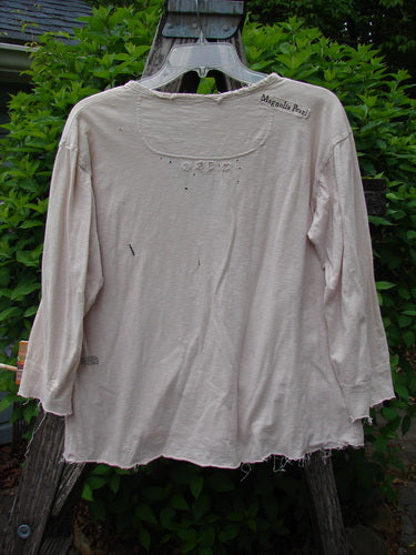 Magnolia Cotton Jersey Tobacco Picker's Henley Tee Tea Stain OSFA displayed with frayed hem, small holes, and faint lettering, draped over a wooden structure against green foliage, highlighting its vintage aesthetic.