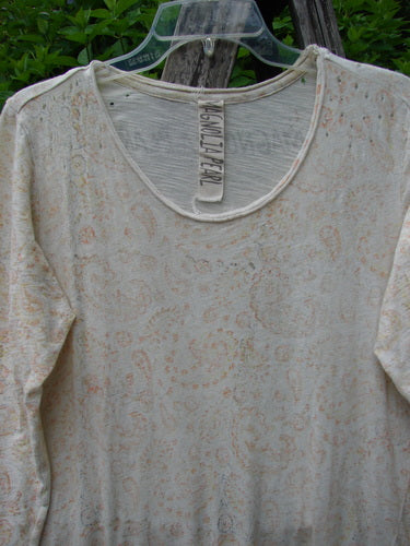 Magnolia Pearl Cotton Dylan Dress Softest Floral Naranja OSFA hangs elegantly on a clear hanger, showcasing its subtle paisley pattern, rolled neckline, tighter sleeves, and distressed seams against a rustic background.