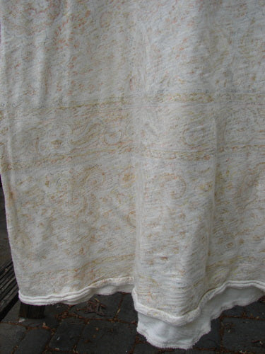 Magnolia Pearl Cotton Dylan Dress Naranja OSFA draped outdoors, showcasing its faint paisley-like print on lightweight fabric, highlighting features like a rolled neckline and roughed seams against a cobblestone surface.