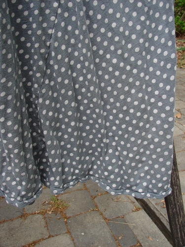 Magnolia Pearl Cotton Dylan Dress Ozzy Tiny Continuous Polka OSFA drapes gracefully over a wooden bench, showcasing its lightweight cotton jersey fabric with white polka dots and raw, roughed-up seams.