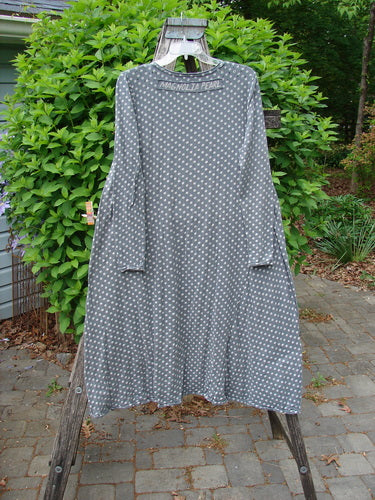 Magnolia Pearl Cotton Dylan Dress Ozzy Tiny Continuous Polka OSFA hangs on a wooden hanger over a stepladder, showcasing its loose fit, raw seams, and unique distressing amidst a garden setting.