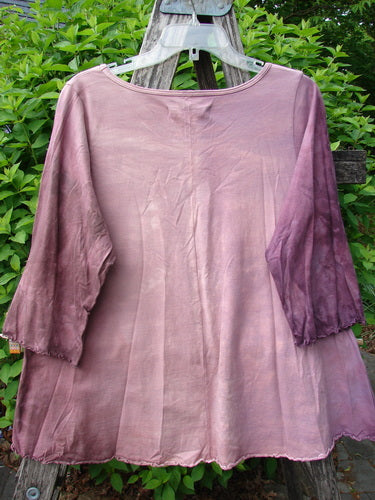 Barclay Three Quarter Sleeved Cafe Tee Alphabet Mottled Peony Size 0: A gently flared mauve blouse with a round neckline, three-quarter sleeves, and sweet curly edgings, hanging on a rustic ladder.
