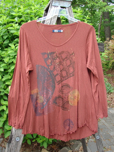 Barclay Modal Long Sleeved A Lined Tee Fall Woods Cassia Size 0, featuring a scooped neckline, gathered cuffs, and abstract front print, displayed on a ladder against outdoor greenery.