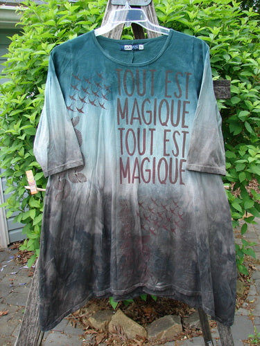 Barclay Wander Tunic Tee Magic Mottled Vintage Teal Size 0, featuring tie-dyed green to gray tones, TOUT EST MAGIQUE text, and bird graphics, hangs outdoors, showcasing its long, loose fit and three-quarter sleeves.