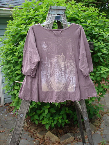 Barclay Crop A Lined Cafe Tee, Potted Floral City Moonlight theme, is draped on a ladder. This loose-fitting mauve top features elbow-length sleeves, a rounded neckline, and curly edgings.