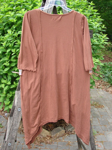 Barclay Wildflower Tunic Floral Sprig Harvest Size 0 draped on a ladder, showcasing its loose fit, raw-edged front, dippy sides, flutter hemline, and three-quarter sleeves in a garden setting.