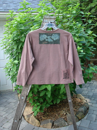 1994 PMU Patched Long Sleeved Tee Rosewood Size 1 displayed on a wooden rack, showcasing patches with playground and cloud themes, a rolled neckline, and a slightly shortened hemline.