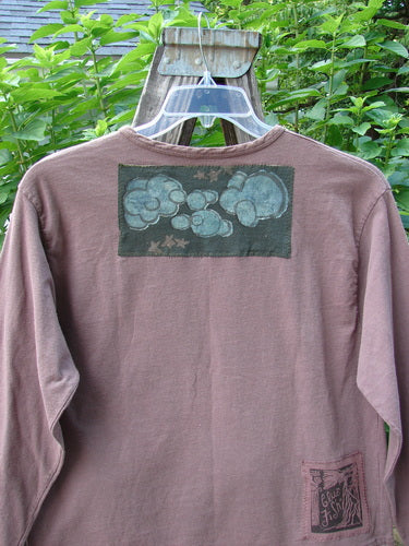 1994 PMU Patched Long Sleeved Tee Rosewood Size 1 displayed on a hanger, featuring a rolled neckline, shortened hemline, cozy long sleeves, and significant playground and cloud-themed patches.