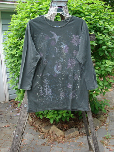 Barclay Long Sleeved Studio Tee Moon Gull Garden Ash Black Size 0, features a forest-green color with a nature motif, draped on a stepladder, showcasing its whimsical, boxy design.