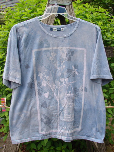 Barclay Fiona Crop Straight Tee Victorian Mottled Bluestone Size 0, adorned with a stylized tree graphic featuring leaves, hearts, and birds, displayed on a hanger outdoors, embodying Bluefishfinder.com’s vintage-inspired, expressive fashion ethos.