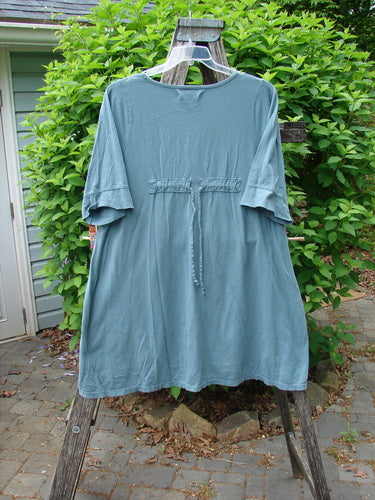 Barclay Three Quarter Sleeved Happiness Tunic Floral Notes Dusty Sky Size 0, featuring a drawcord back, elbow-length sleeves, empire waist tie, and asymmetrical hem, displayed on a wooden ladder.