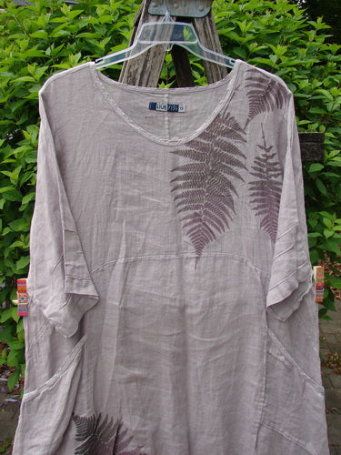 Barclay Linen Wave Pocket Dress Fern Mallow Quartz Size 0: Light-taupe tunic with fern-leaf print, scooped neckline, elbow-length sleeves, two side pockets, hanging on a wooden ladder against foliage.