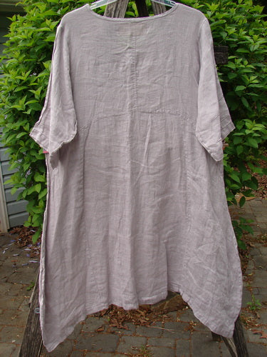 Barclay Linen Wave Pocket Dress Fern Mallow Quartz Size 0: Oversized light gray linen tunic with round neckline, elbow-length sleeves, A-line cut, front pockets, and varying hemline, hanging outdoors.