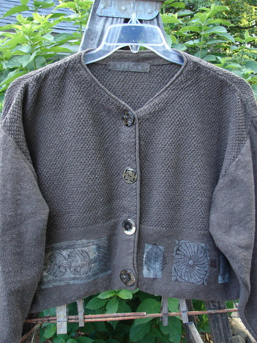 1994 Crop Cardigan Sweater Topiary Humus OSFA displayed on a wooden swing, showcasing its V-shaped neckline, dual contrasting knits, stoneware buttons, and cozy longer sleeves with dropped shoulders.