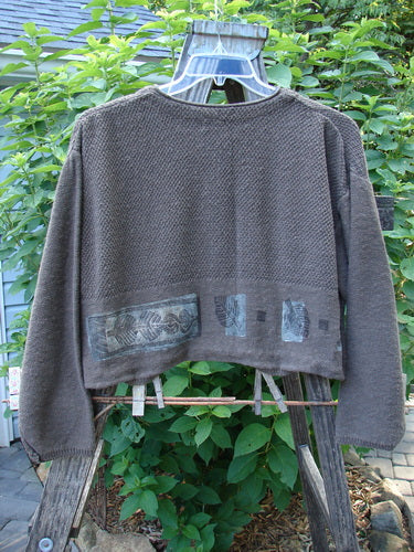 1994 Crop Cardigan Sweater Topiary Humus OSFA displayed on a swing, highlighting its variegated texture, stoneware buttons, V-shaped neckline, cozy longer sleeves, and dropped shoulders.