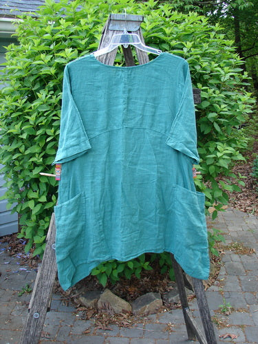 Barclay Linen Side Pocket Urchin Dress Chair Note Jade Size 0, featuring a round neckline, elbow-length sleeves, empire waist, and unique wrap-around drop pockets, displayed outdoors over a wooden ladder.