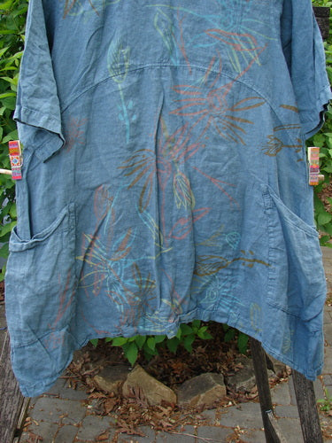 Barclay Linen Side Pocket Urchin Dress Mixed Tulip Garden Dusty Sky Size 0 displayed with dropped shoulders, elbow-length sleeves, and hand-drawn botanical motifs, hanging outdoors on a drying rack.