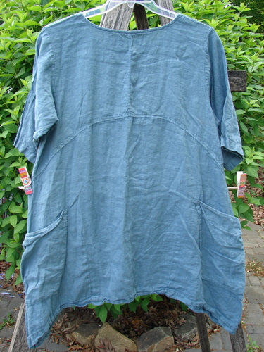 Barclay Linen Side Pocket Urchin Dress in Dusty Sky features short sleeves, a round neckline, and large side pockets, hanging on a wooden ladder, embodying Bluefishfinder.com's vintage charm.