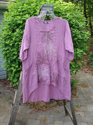 Barclay Linen Posey Dress Tiny Floral Orchid Size 0, featuring elbow-length sleeves, scoop neckline, front patch pockets, and a subtle decorative texture, displayed hanging on a ladder amidst outdoor greenery.