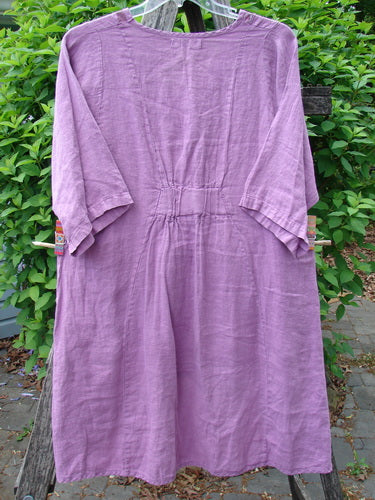 Barclay Linen Posey Dress Tiny Floral Orchid Size 0, featuring a loose-cut, knee-to-mid-calf length with ¾-length sleeves, oval neckline, and curvy panels, draped on a hanger against greenery.