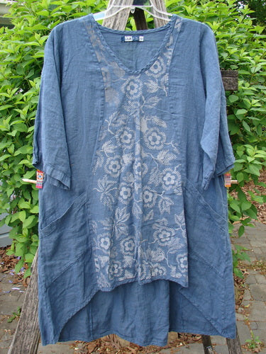 Barclay Linen Posey Dress Daisy Ray Blue Echo Size 0, displayed on a hanger, showcases elbow-length sleeves, V-neck, floral front panel, and high-low hem against green shrubbery.