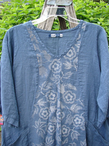 Barclay Linen Posey Dress Daisy Ray Blue Echo Size 0 features a slate-blue linen tunic with three-quarter sleeves, scoop neckline, and floral print panel, elegantly draped over a wooden trellis.