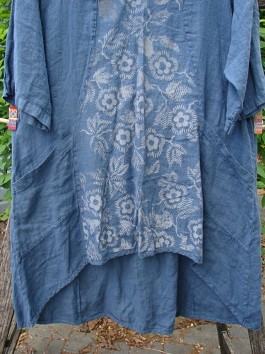 Barclay Linen Posey Dress Daisy Ray Blue Echo Size 0, featuring a knee-length, smock-style with floral panel, rolled-up sleeves, and side pockets, hanging against a green wire fence outdoors.