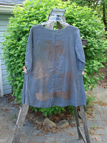 Barclay Linen Lucida Top Metallic Fern Blue Storm Size 0, hanging elegantly on a wooden stepladder, showcases ¾-length gathered sleeves and a round neckline, embodying Bluefishfinder.com's vintage-inspired style.