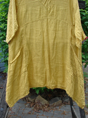 Barclay Gauze Linen Cross Over Dress Unpainted Sunshine Spice Size 1, showcasing a crinkled texture with a V-neck, drop shoulders, elbow sleeves, asymmetrical hem, and double side pockets, hanging outdoors.