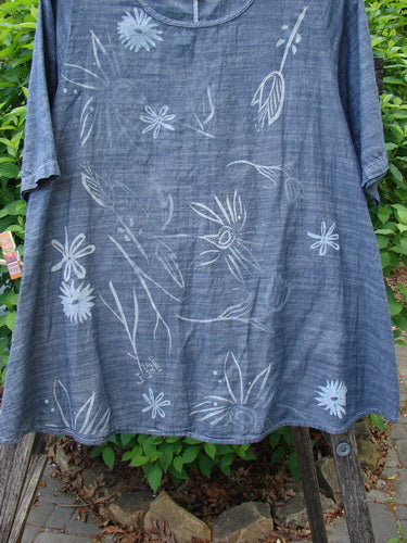 Barclay Chambray Short Sleeved Top Floral Joy Dark Denim Striation Size 0, featuring a sketch-like white floral motif on a lightweight, A-line design, displayed outdoors against a natural backdrop.