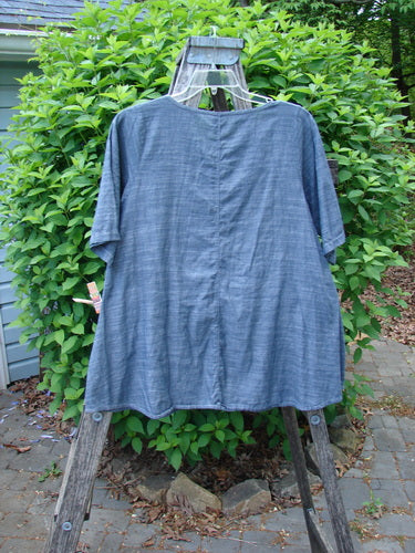Barclay Chambray Short Sleeved Top Floral Joy Dark Denim Striation Size 0 draped on a wooden stepladder, showcasing its A-line shape, rounded neckline, and lightweight lawn cotton texture.