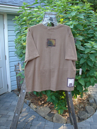 1998 Men's Short Sleeved Tee Sailboat Rock Brown Size 2 XL displayed on a wooden clothes rack, showcasing a sailboat theme paint and a softly thicker ribbed neckline.