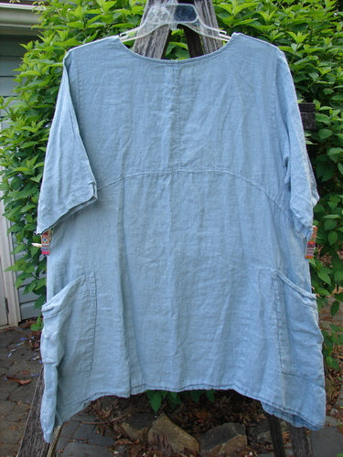Barclay Linen Urchin Dress Leaf Floral Dusky Watercolor Size 1: A loose-fitting, light-blue tunic with rounded neckline, short sleeves, curved empire waist, varying side lengths, and two hip patch pockets.