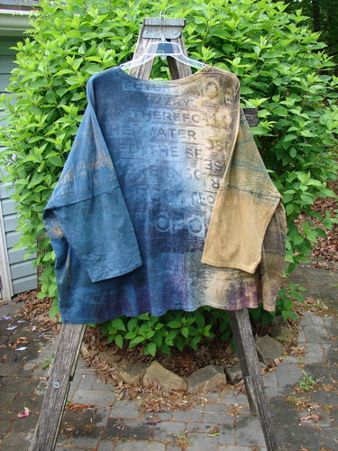 Barclay Writer's Pocket Pullover Future Night to Day OSFA draped on a wooden ladder, showcasing its seamless design, dynamic art, and rounded neckline with dual pockets against a lush outdoor backdrop.