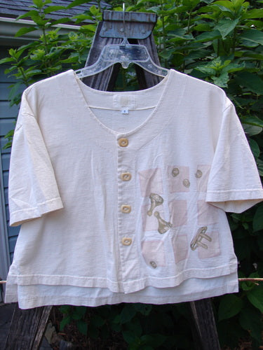 2001 Button Crop Top Pawn Natural Size 0: A white crop top with wide short sleeves, featuring a chess game theme paint and unique buttons, displayed on a hanger.