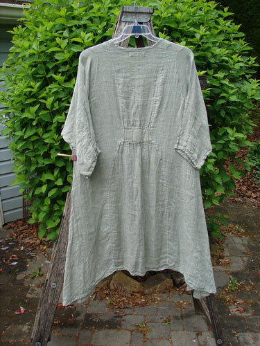 Barclay Linen High Vent Venetian Dress Contour Floral Sage Size 1, displayed on a hanger over a wooden ladder, features a gathered waist, elbow-length sleeves, and varying hemline, embodying Bluefishfinder.com's vintage charm.