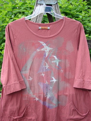 Daisy Hagey Barclay Banded Artist Pocket Top Metallic Bird Flight Rust Size 1 in rust-colored fabric, with a metallic bird flight graphic, three-quarter sleeves, and front pockets hanging on a clear hanger outdoors.