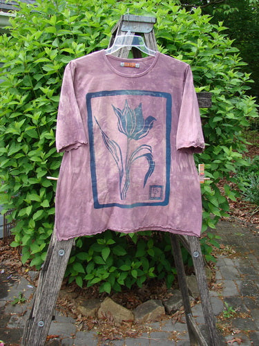 Barclay Cotton Lycra Three Quarter Sleeved Cafe Tee Single Tulip Mottled Mauve Size 1 displayed on a wooden stepladder, showcasing its tulip graphic and unique A-line shape amidst a garden setting.