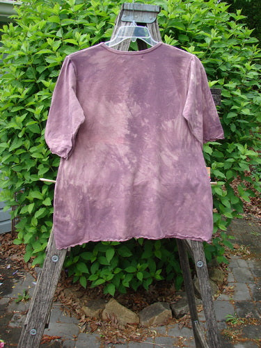 Barclay Cotton Lycra Three Quarter Sleeved Cafe Tee displayed on a hanger against a wooden ladder, showcasing its unique mottled mauve design, elbow-length sleeves, and A-line shape in an outdoor setting.