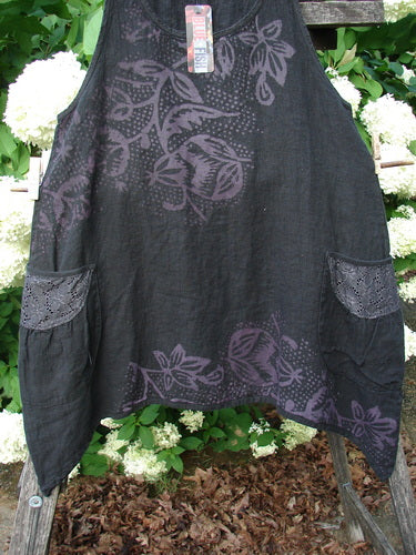 Bluefishfinder.com Barclay NWT Summercloth Lace Two Pocket Pinafore Floral Fern Black Size 0, a black pinafore with purple floral fern print, lace-trimmed side pockets, and a soft, textured summercloth finish. It hangs centered against leafy white flowers and wood, with natural outdoor light deepening the dark fabric and pattern.