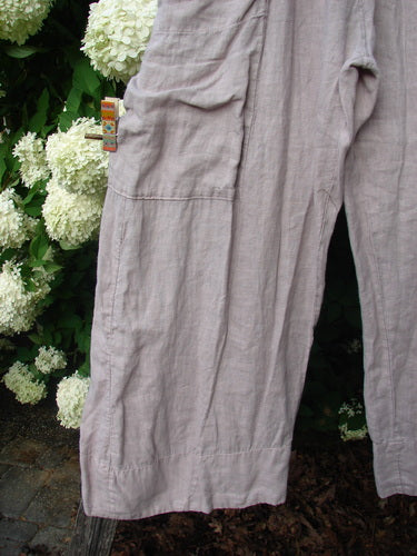 Bluefishfinder.com Barclay Linen Single Side Pocket Banded Bottom Pant in unpainted mallow, size 0, shown in soft linen with a loose, crinkled drape. The cropped view highlights a single side pocket, banded hems, and a pale mauve-gray tone against leafy white hydrangeas.